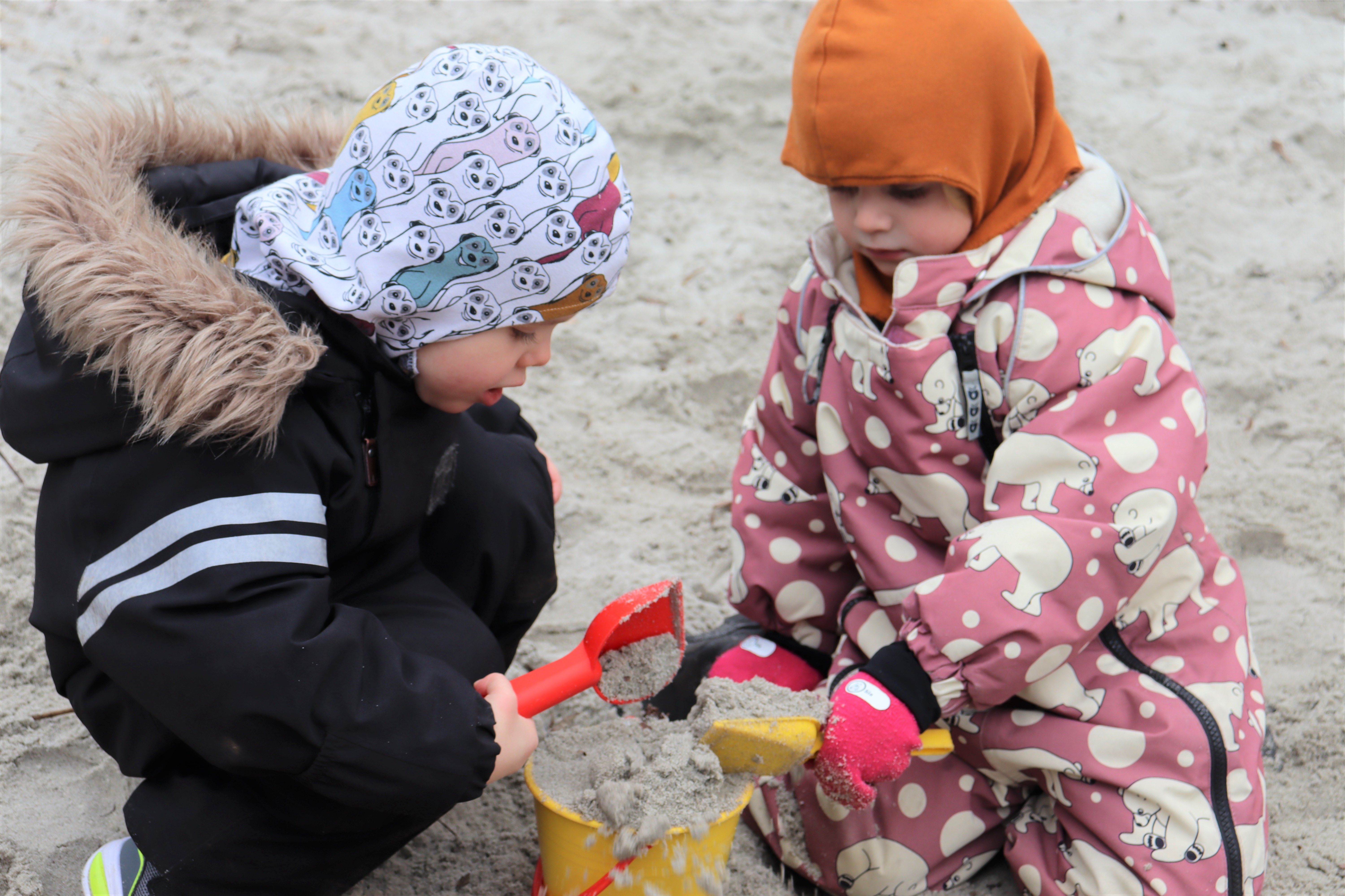 To børn er i sandkasse og leger med sand i spande
