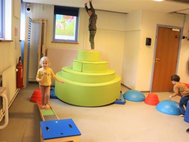 Aktivitetsrum med balancebom, pudeborg og baner, hvor børn går rundt på alle tingene